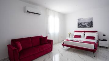 A modern hotel room with a red sofa, a bed with white bedding, a marble floor, and a cityscape view.