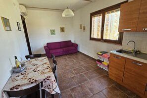 Een compacte keuken met een eettafel, een paarse bank en een raam met gordijnen.