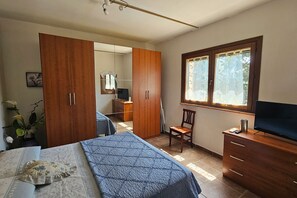 Een slaapkamer met een bed, een dressoir, een televisie, een stoel en een raam.