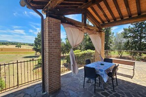 An outdoor patio with a table and chairs, a brick column, and a view of a vineyard. - Apartment Roggiano Tuscan countryside with pool (Scansano)