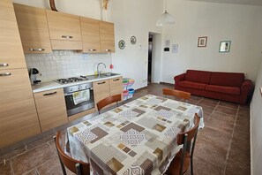 A kitchen with wooden cabinets, a stove, and a dining table with a patterned tablecloth. - Apartment Sicomoro, pool and countryside (Scansano)