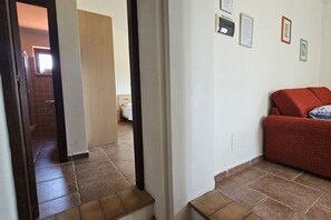 A hallway with a staircase leading to a bedroom, a red sofa, and a wall with framed pictures. - Apartment Sicomoro, pool and countryside (Scansano)