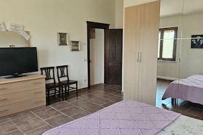 A room with a television, two chairs, a bed, a wardrobe, and a door. - Apartment Sicomoro, pool and countryside (Scansano)