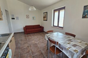 A dining area with a table, chairs, a sofa, and a window with curtains. - Apartment Sicomoro, pool and countryside (Scansano)