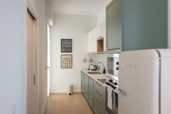 Eine moderne Küche mit Kühlschrank, Backofen und Spüle. An den Wänden hängen botanische Bilder in Rahmen.