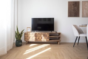 Ein modernes Wohnzimmer mit einem Flachbildfernseher auf einer Holzkommode, einer Topfpflanze und einem gerahmten Bild an der Wand.