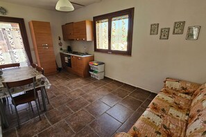 A compact kitchen with wooden cabinets, a dining table with chairs, a sofa, and a window with curtains. - Apartment Benefizio, pool and tuscan nature (Scansano)
