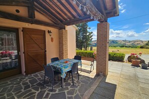 An outdoor patio with a table and chairs, a wooden door, and a view of the countryside. - Apartment Benefizio, pool and tuscan nature (Scansano)