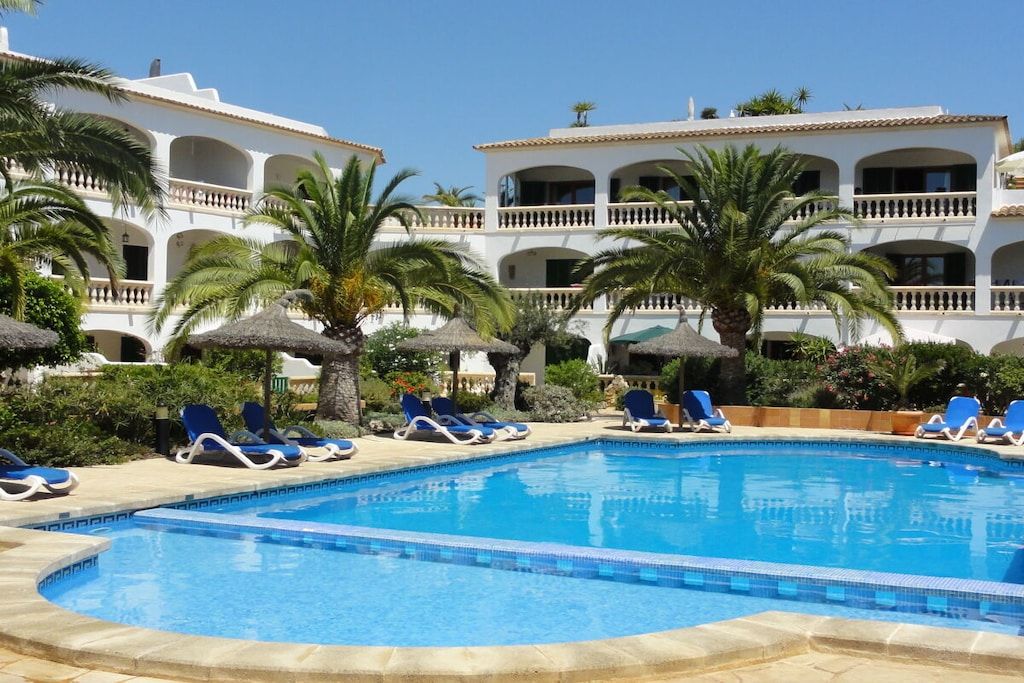 A pool area with lounge chairs and a building with balconies.