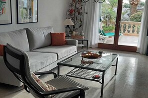 A living room with a sofa, armchair, coffee table, and a balcony with outdoor furniture. - Holiday apartment with 1 bedroom (Cala  Santanyi)