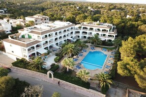 A multi-story hotel with a central courtyard, a swimming pool, and palm trees. - Holiday apartment with 1 bedroom (Cala  Santanyi)