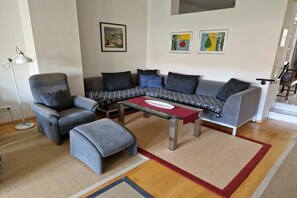 A modern living room with a sectional sofa, a small armchair, and a glass coffee table. - Holiday apartment with 1 bedroom (Endingen-Königschaffhausen)