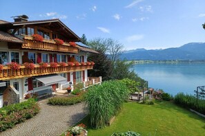 Ein zweistöckiges Chalet mit Balkon, Stein Fundament und Blick auf See und Berge.