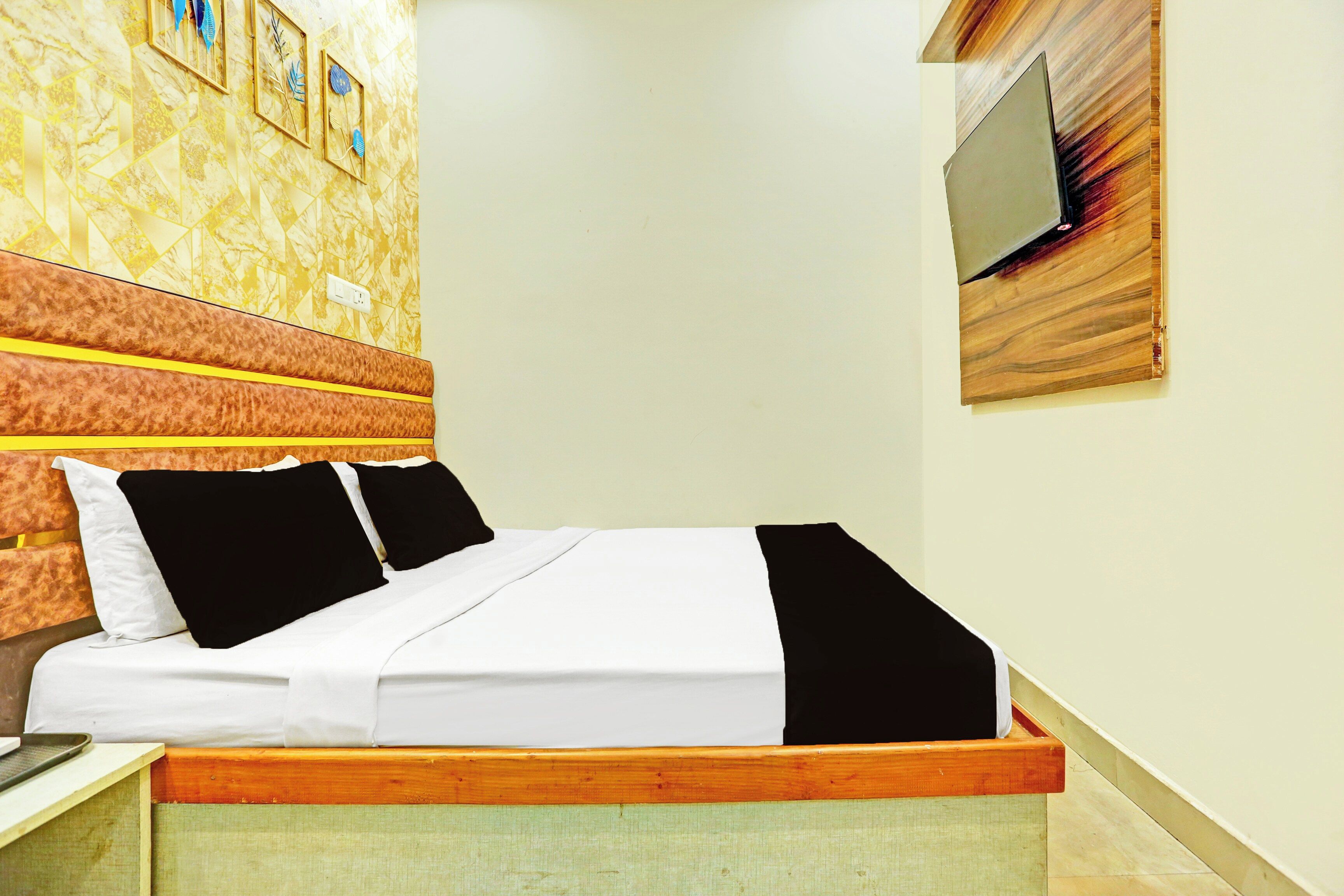 Quarto de hotel com cama, televisão presa à parede e papel de parede estampado.