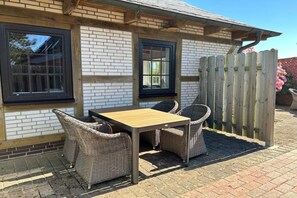 A patio with a table and wicker chairs, a wooden fence, and a brick wall. - Holiday home with 2 bedrooms (Büsumer-Deichhausen)