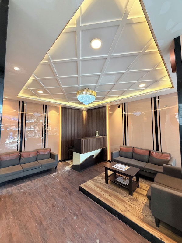 A modern interior with a reception desk, two sofas, a coffee table, and a chandelier. - Trishul Inn (Bengaluru)