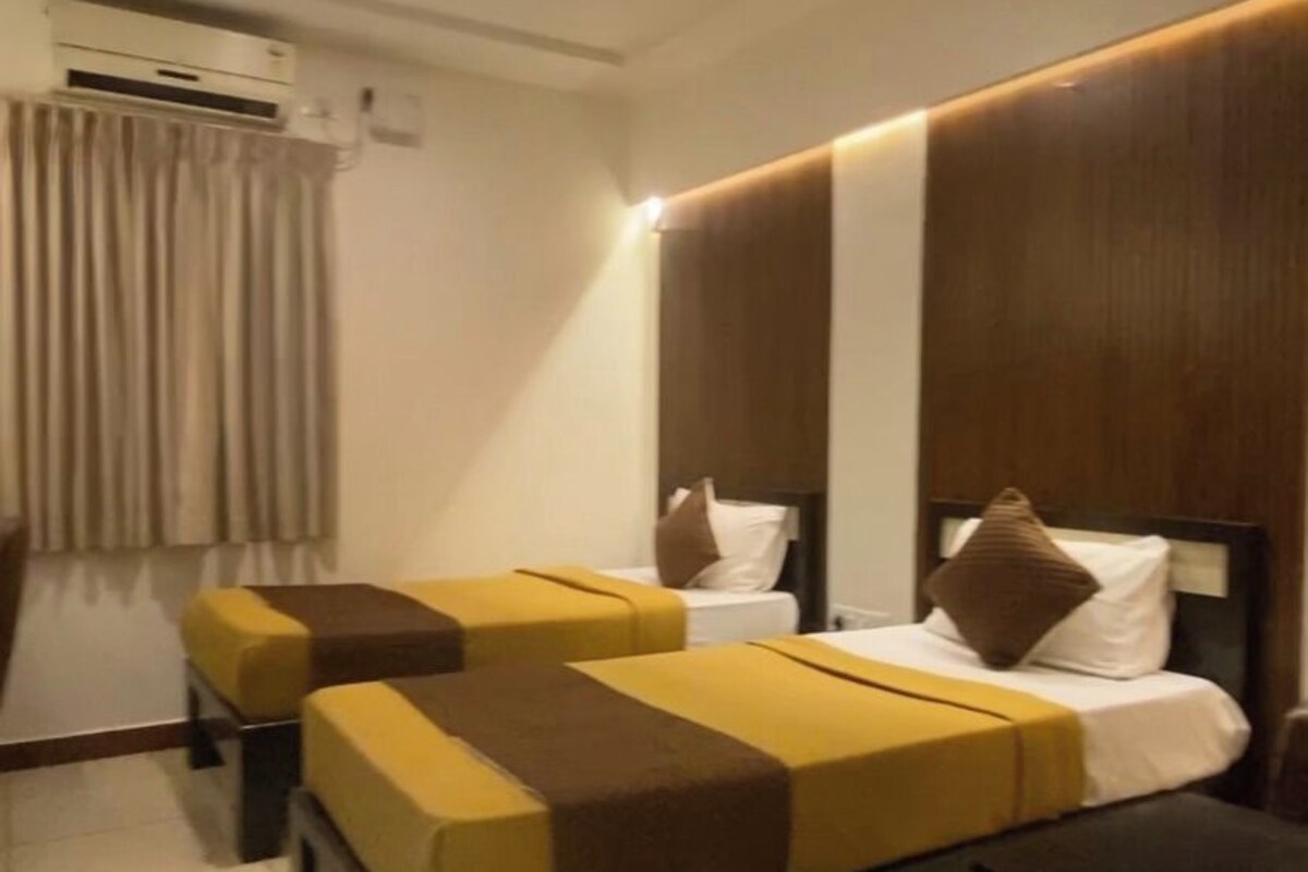 A hotel room with a bed, two bedside tables, a ceiling fan, an air conditioning unit, and a window with curtains.