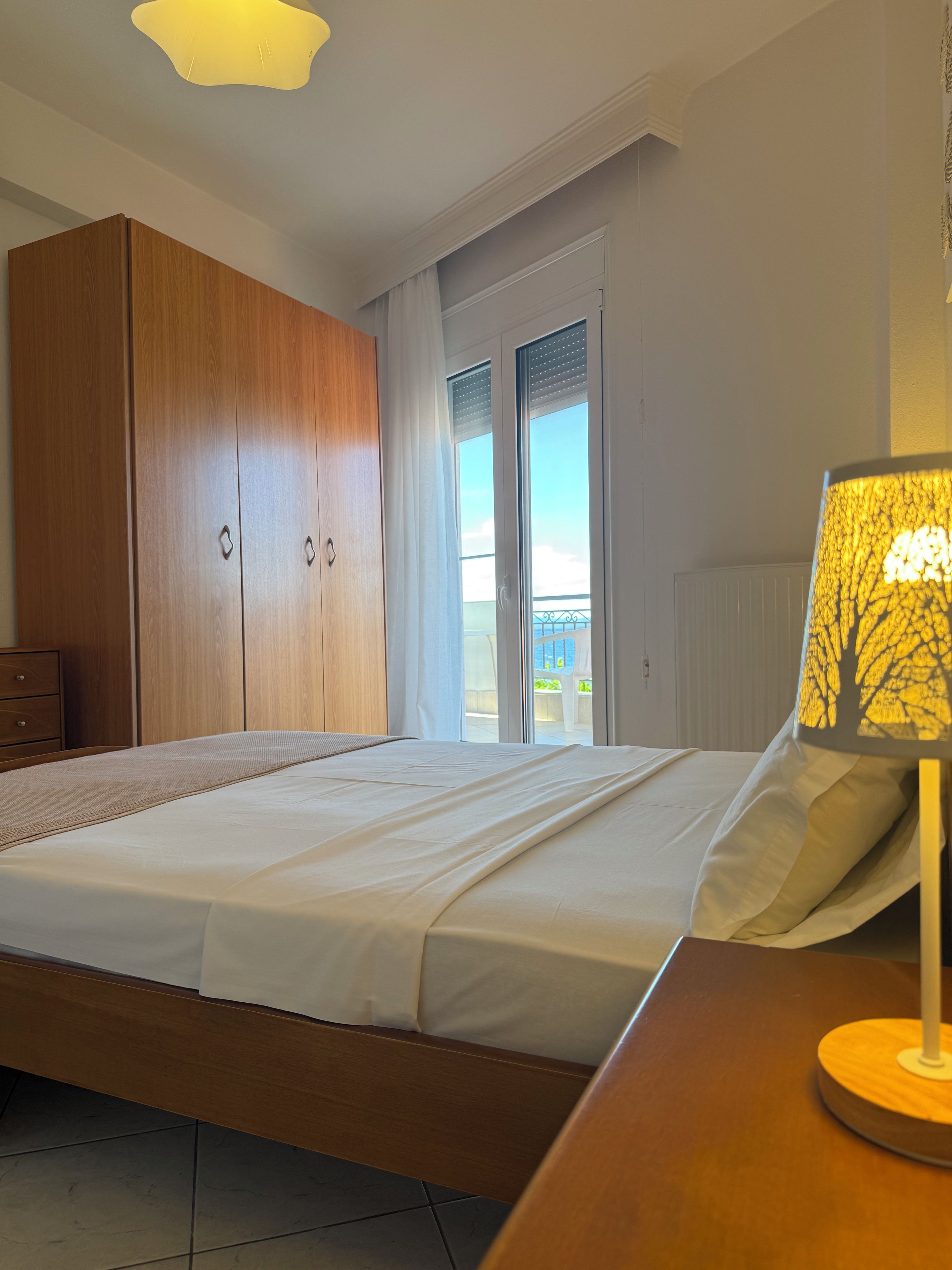 Quarto com cama, guarda-roupa de madeira e vista através de uma porta de vidro.