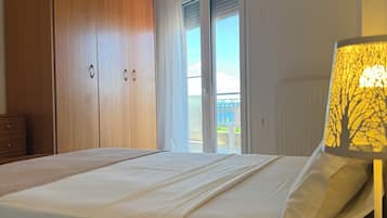 Quarto com cama, guarda-roupa de madeira e vista através de uma porta de vidro.