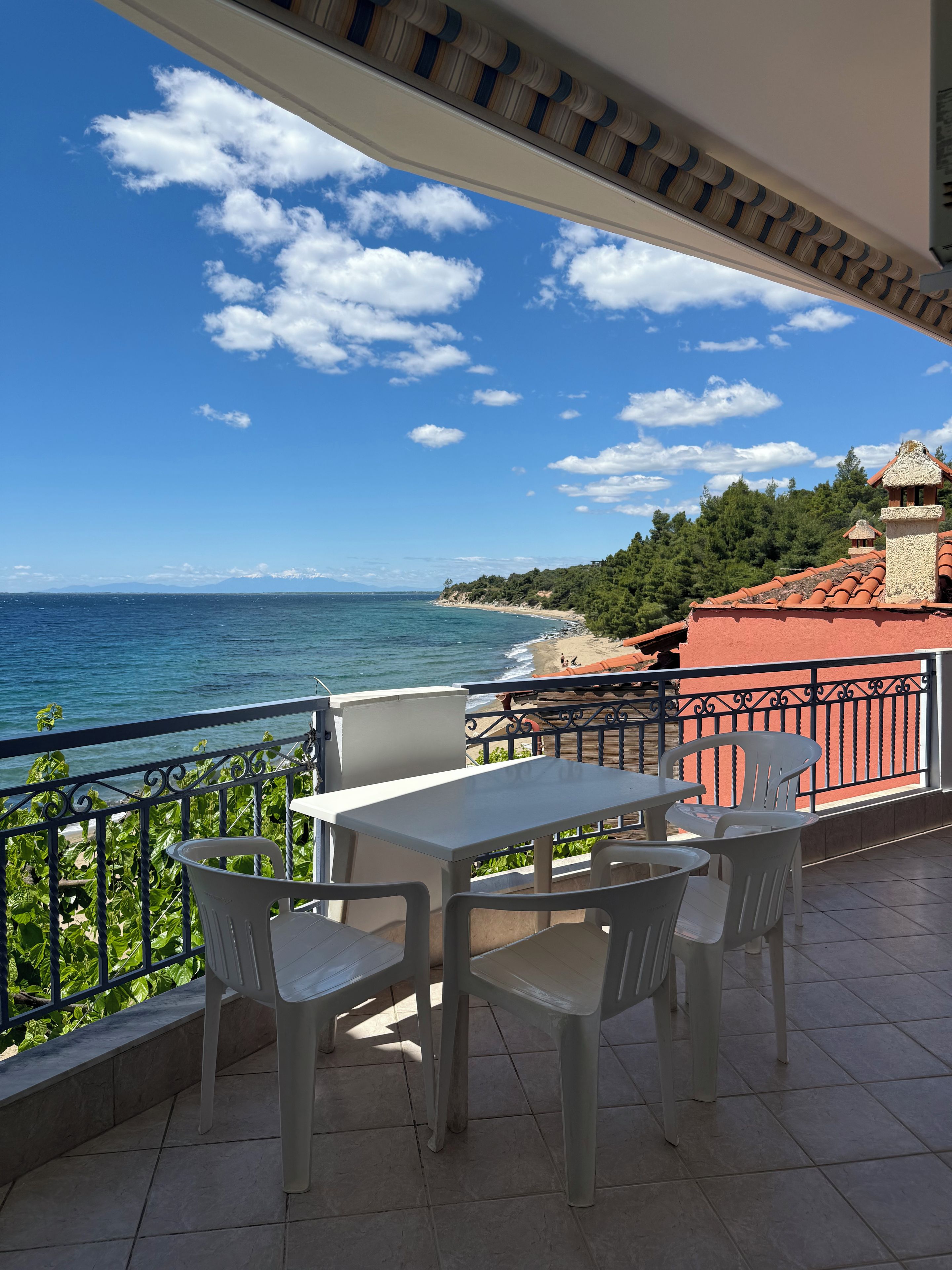 A balcony with a table and chairs, overlooking a beach and the sea.