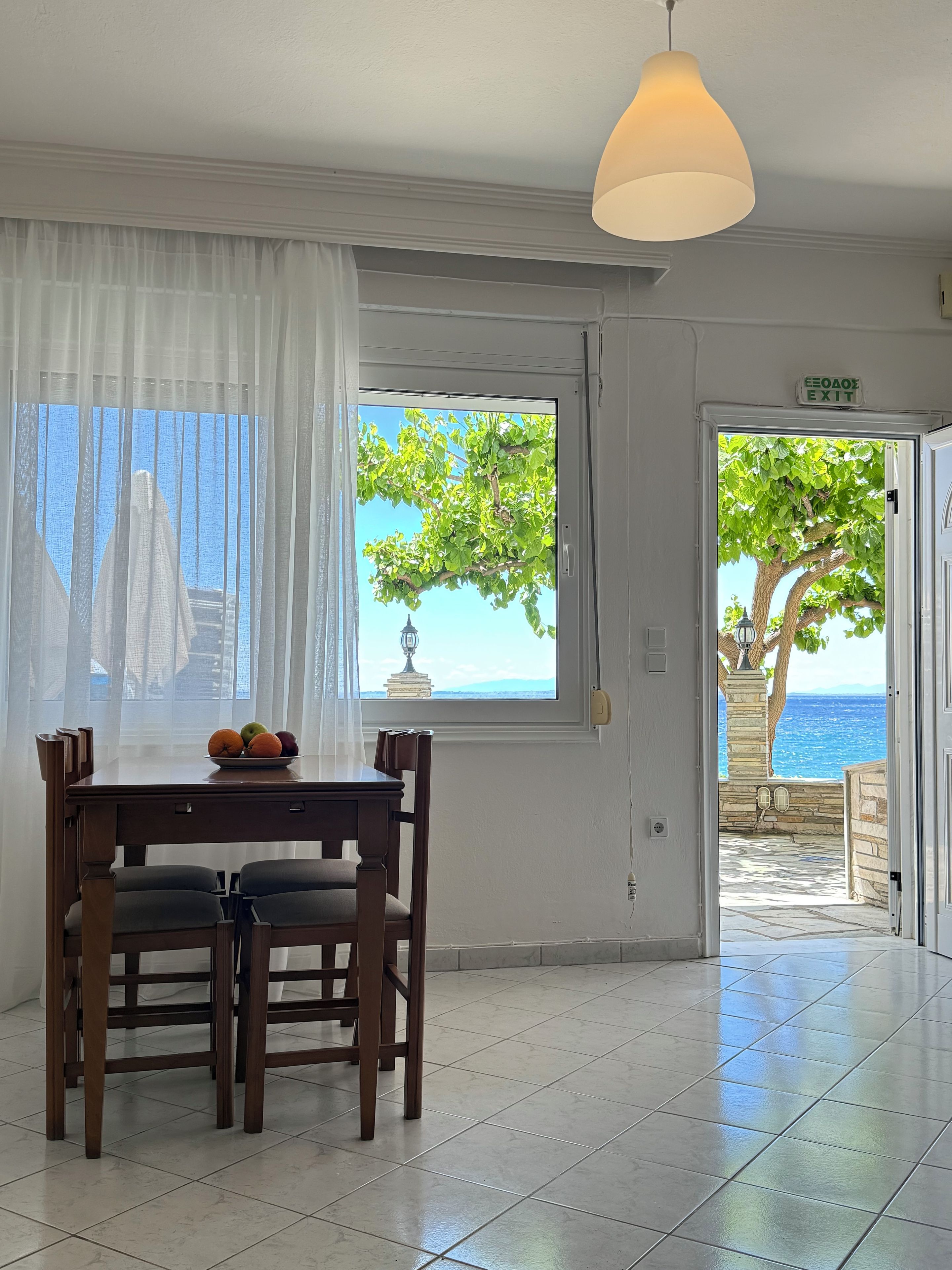 Quarto com mesa de jantar, cadeiras, janela com vista para o mar e luminária pendente.