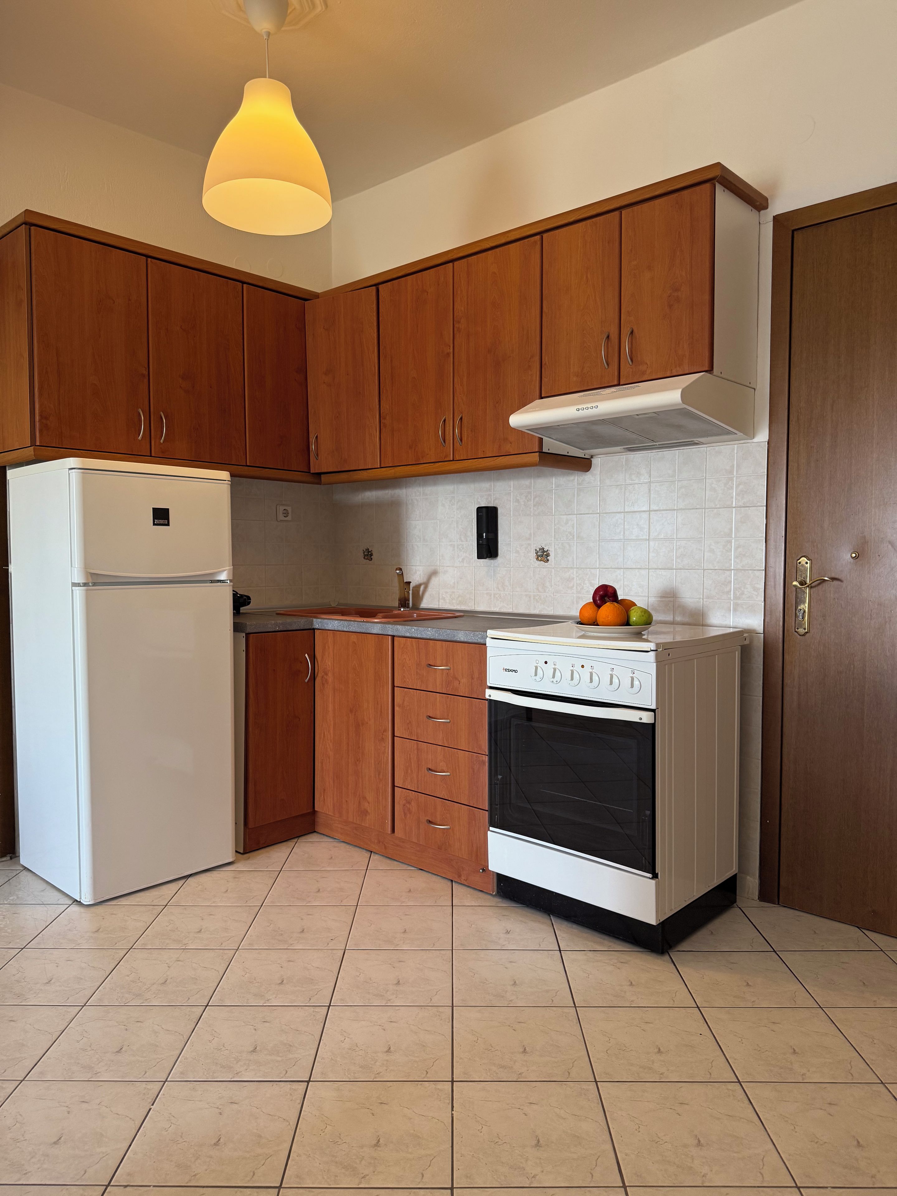 Une cuisine avec des meubles de rangement en bois, un réfrigérateur blanc, une cuisinière et un luminaire suspendu.