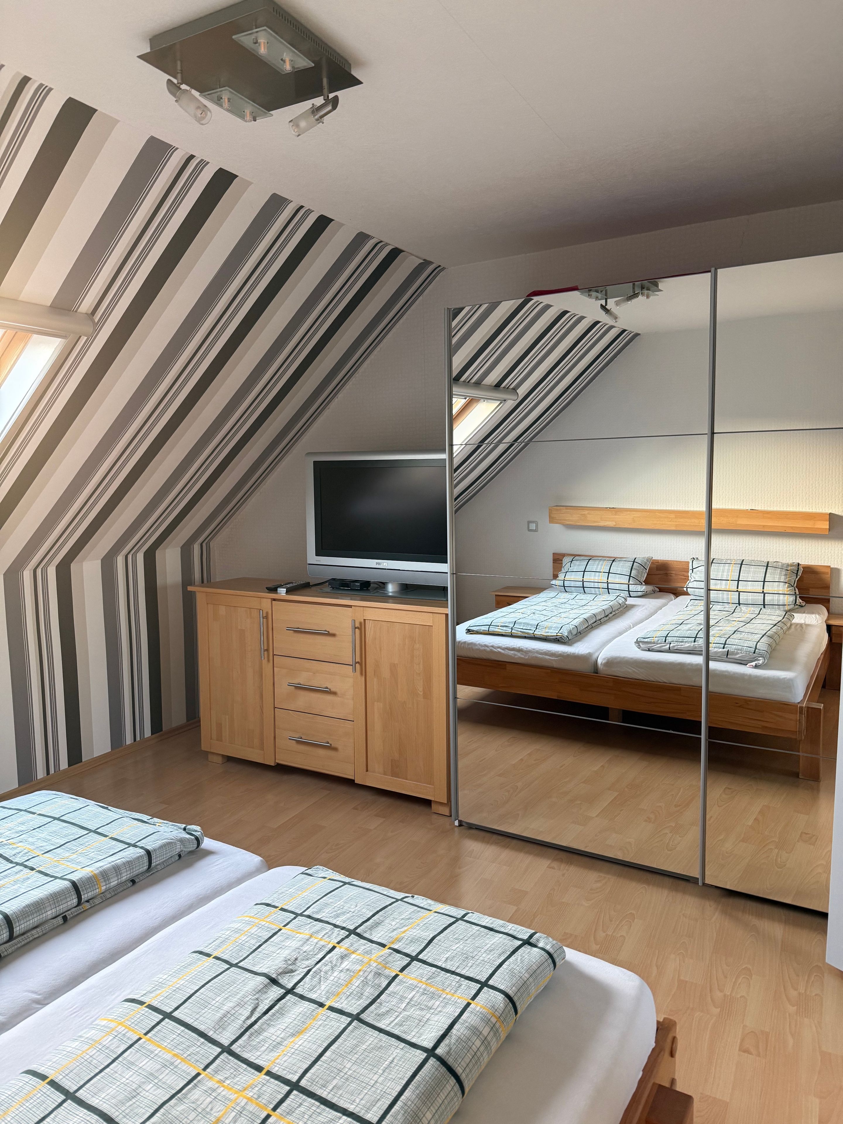 Een slaapkamer met een schuine kap, een bed, een televisie en een kledingkast.