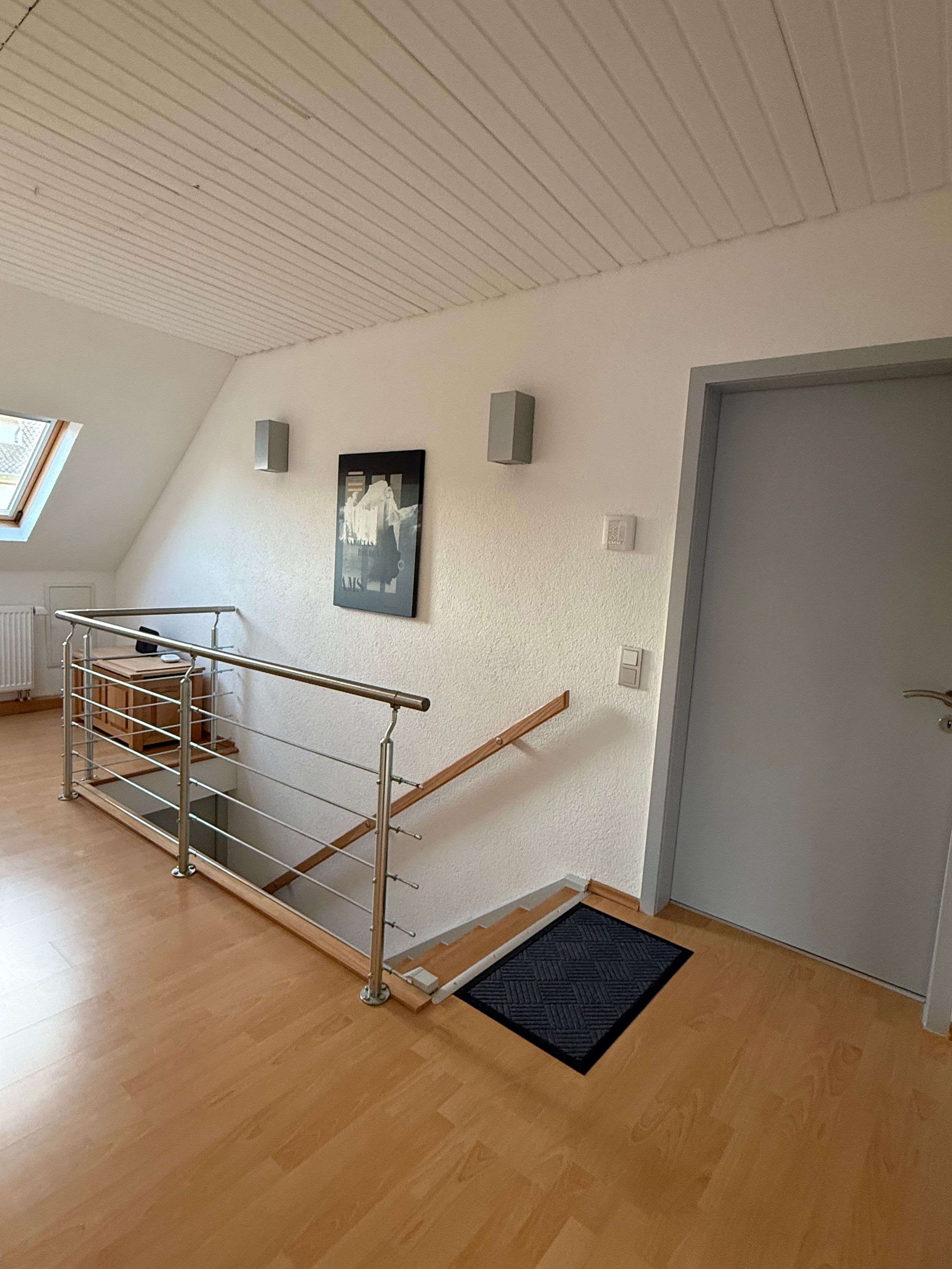 Ein Zimmer mit Holzboden, einer Metall-Spindeltreppe, einer Tür, einem Heizkörper und einem gerahmten Bild an der Wand.