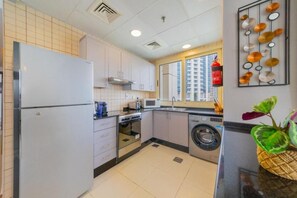 A compact kitchen with a refrigerator, oven, microwave, and washing machine. - Royal Oceanic 2BR with Marina View (Dubai)