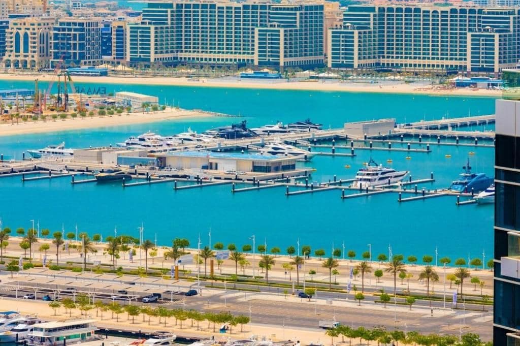 A marina with multiple docks and yachts, surrounded by modern buildings and a clear blue waterfront.