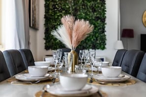 A dining table set with white plates, bowls, and glasses, centered with a decorative vase. - Royal Oceanic 2BR with Marina View (Dubai)