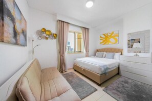 A bedroom with a bed, a sofa, a window with curtains, and a city view. - Royal Oceanic 2BR with Marina View (Dubai)