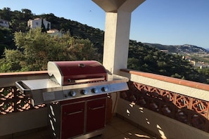 An outdoor grill with a view of a hillside and buildings in the background. - Holiday apartment in Roses with swimming pool (Roses)