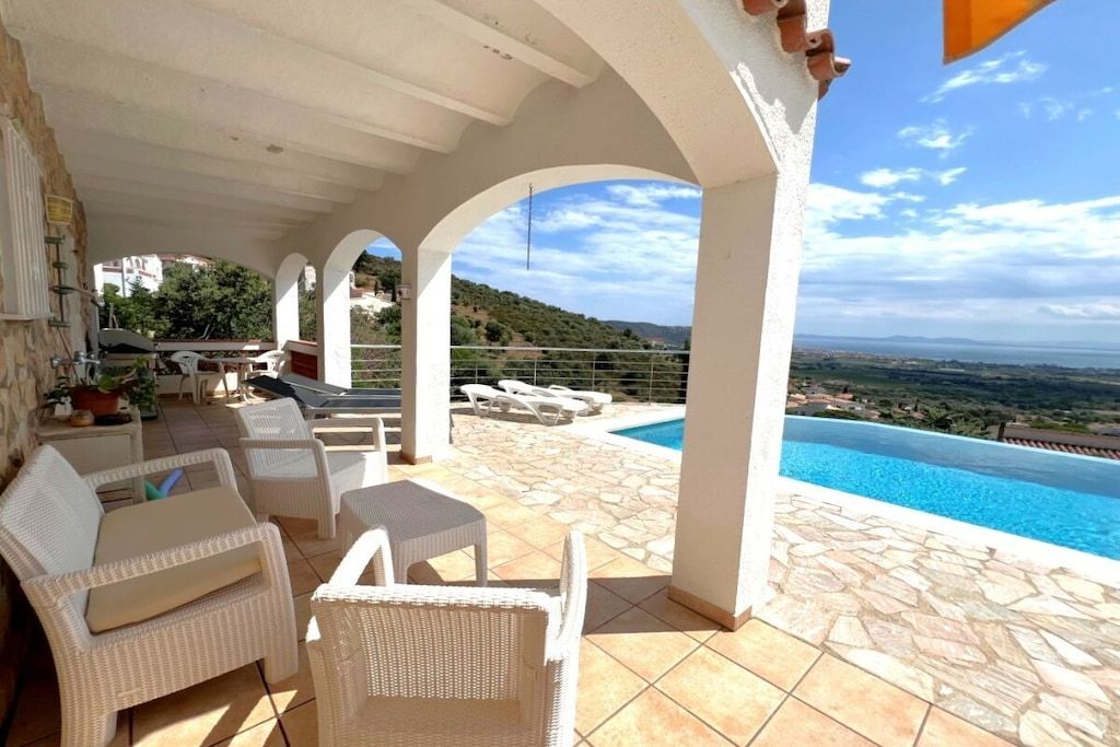A covered outdoor area with a pool, white wicker furniture, and a view of the landscape.