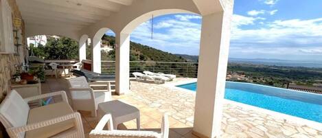 A covered outdoor area with a pool, white wicker furniture, and a view of the landscape.