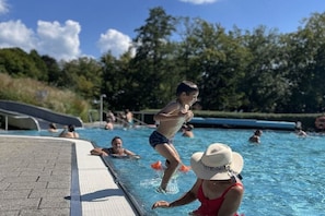 Una piscina con gente nadando y una persona parada en el borde.