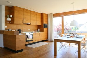 A modern kitchen with wooden cabinets, a central island, and a dining area with a table and chairs. - Holiday apartment with 1 bedroom (Bodolz)