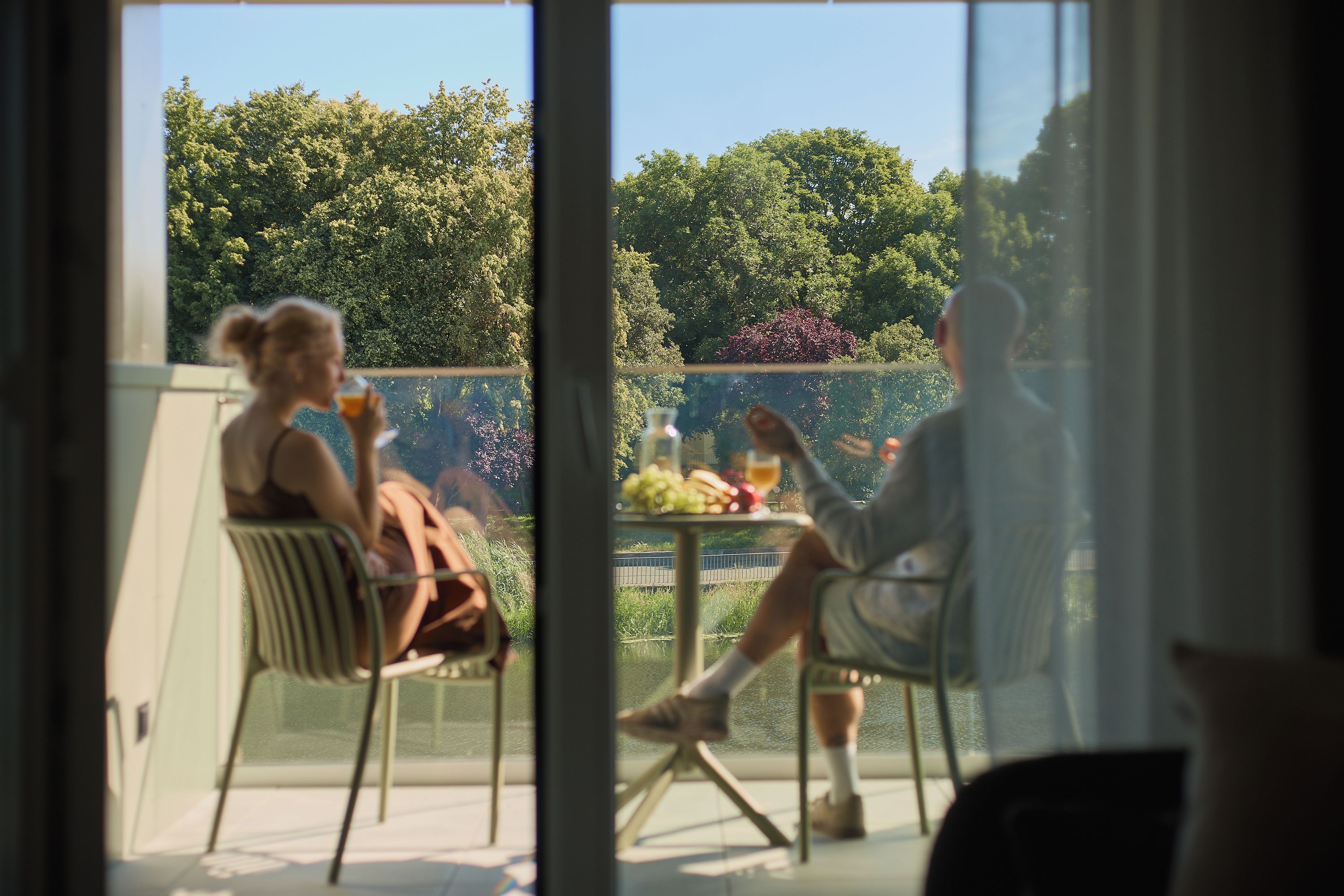 Un balcón con mesa y sillas, con vistas a un jardín con árboles y una valla.