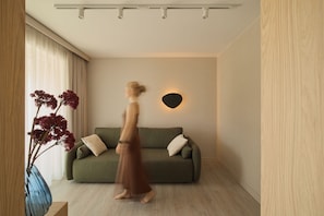 A room with a green sofa, a vase with red flowers, and a wall-mounted light fixture. - Persante Sunrise Collection Marina & River by Downtown Apartments (Kołobrzeg)