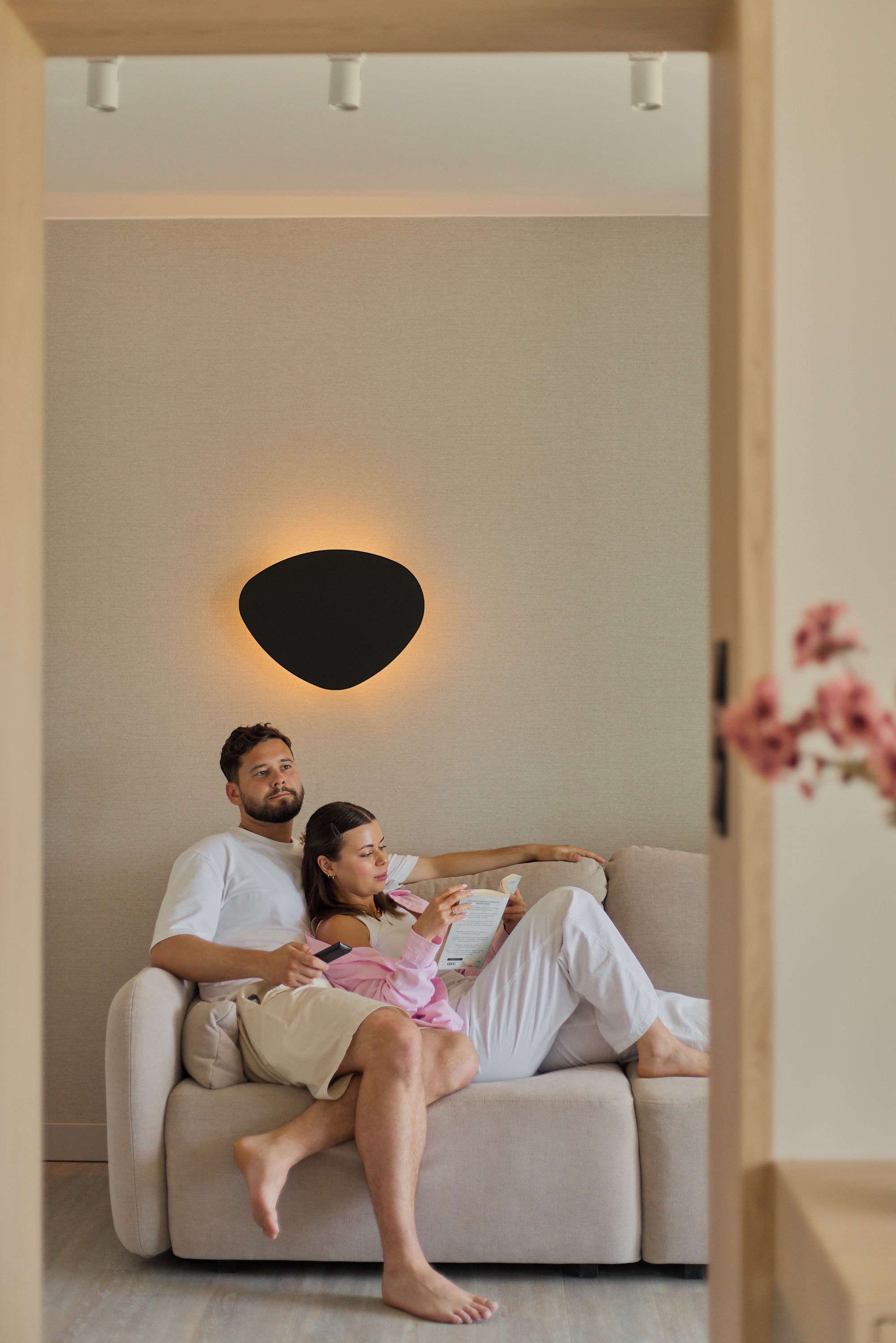 A couple sitting on a sofa in a room with a modern light fixture on the wall.