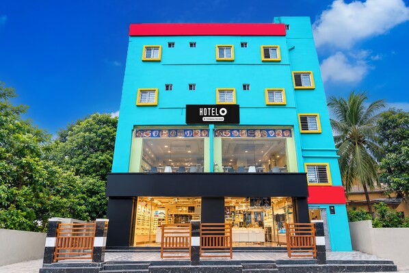 A hotel with a bright blue facade, multiple windows, and a visible restaurant or cafe area with seating.