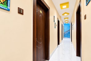 Ein Hotelkorridor mit Holztüren, nummerierten Zimmern und einem blau getönten Glasaufzug.