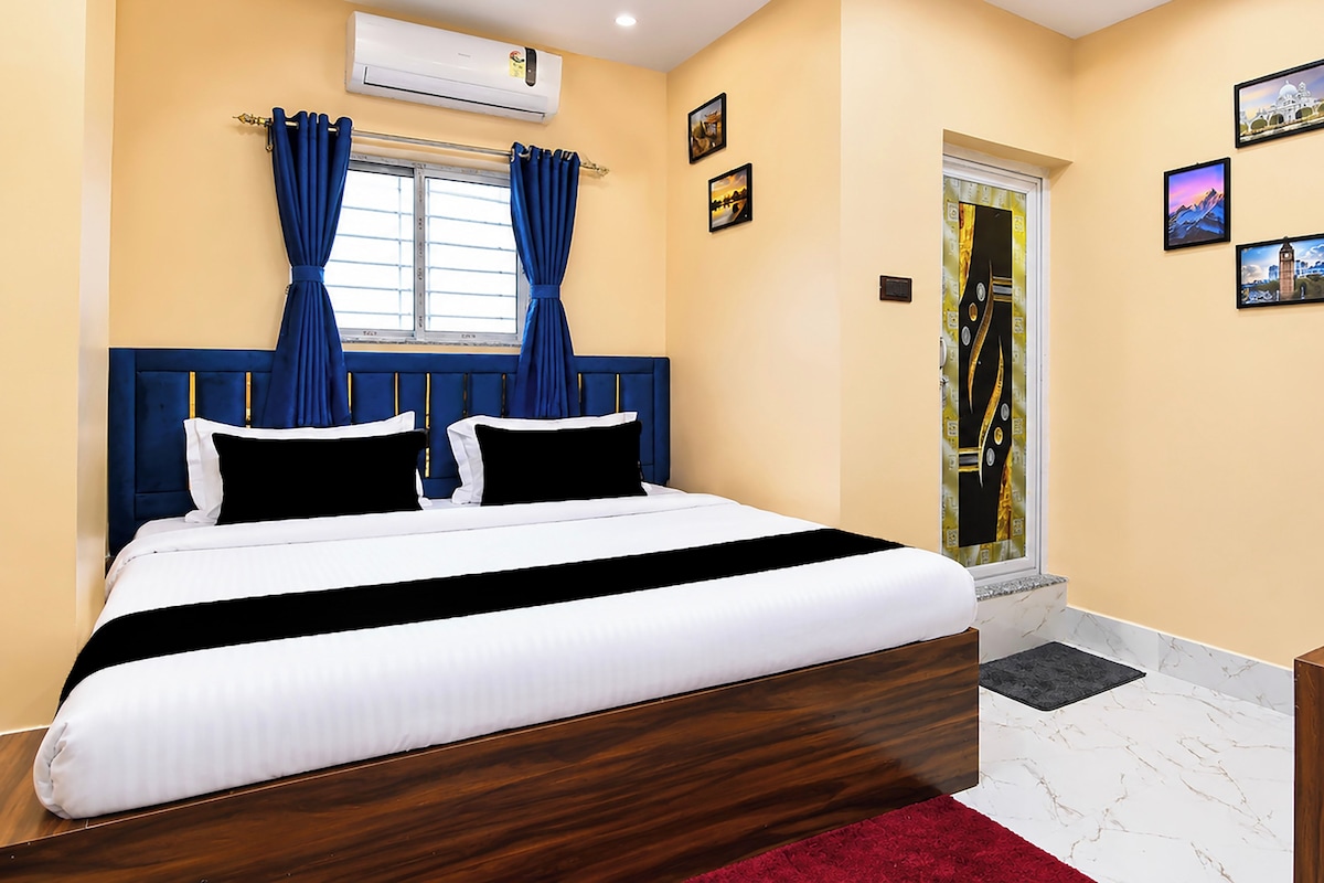 A hotel room with a large bed, a window with curtains, a door with a glass panel, and wall-mounted artwork.