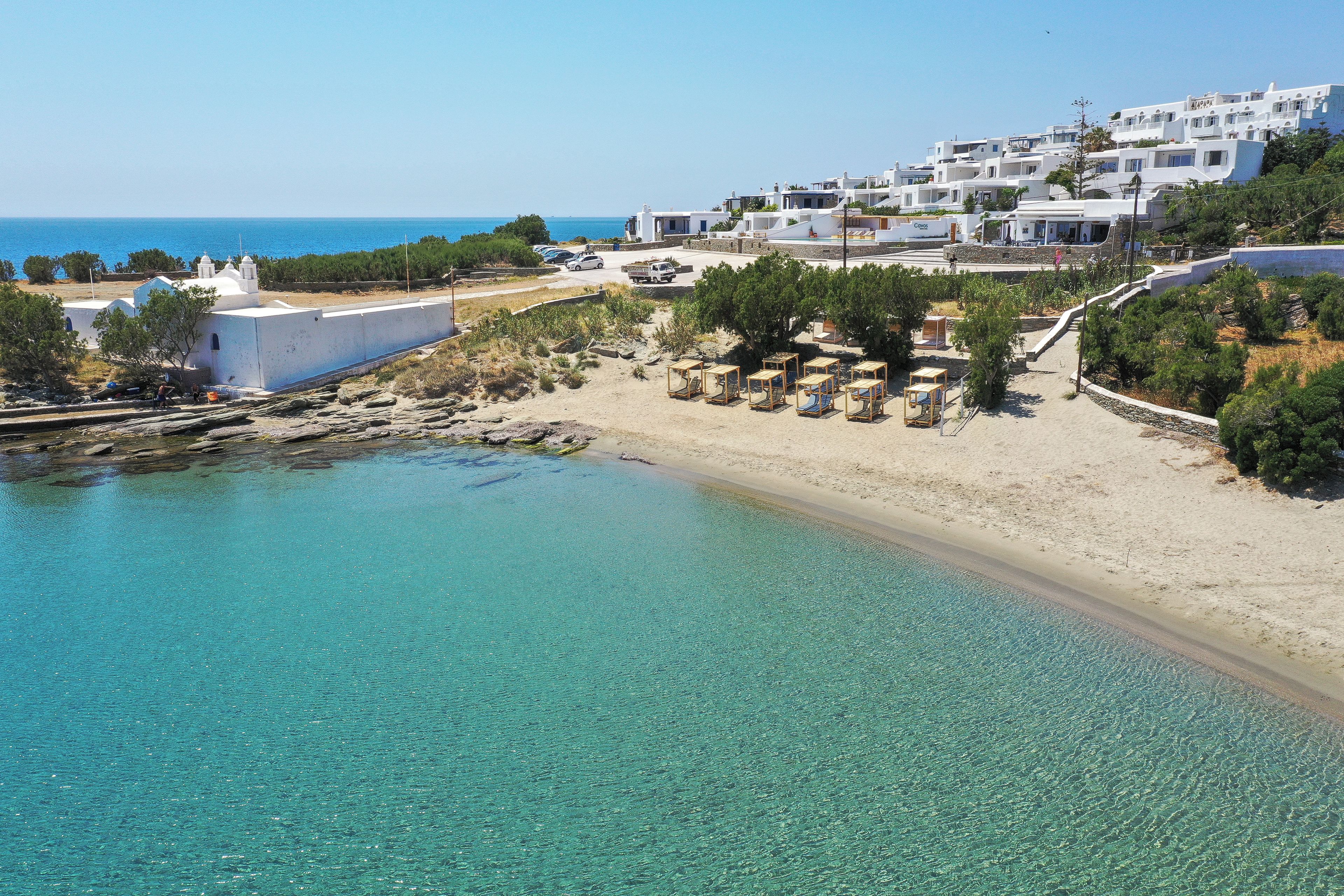 A coastal resort with clear turquoise waters, white buildings, and a sandy beach with sun loungers.