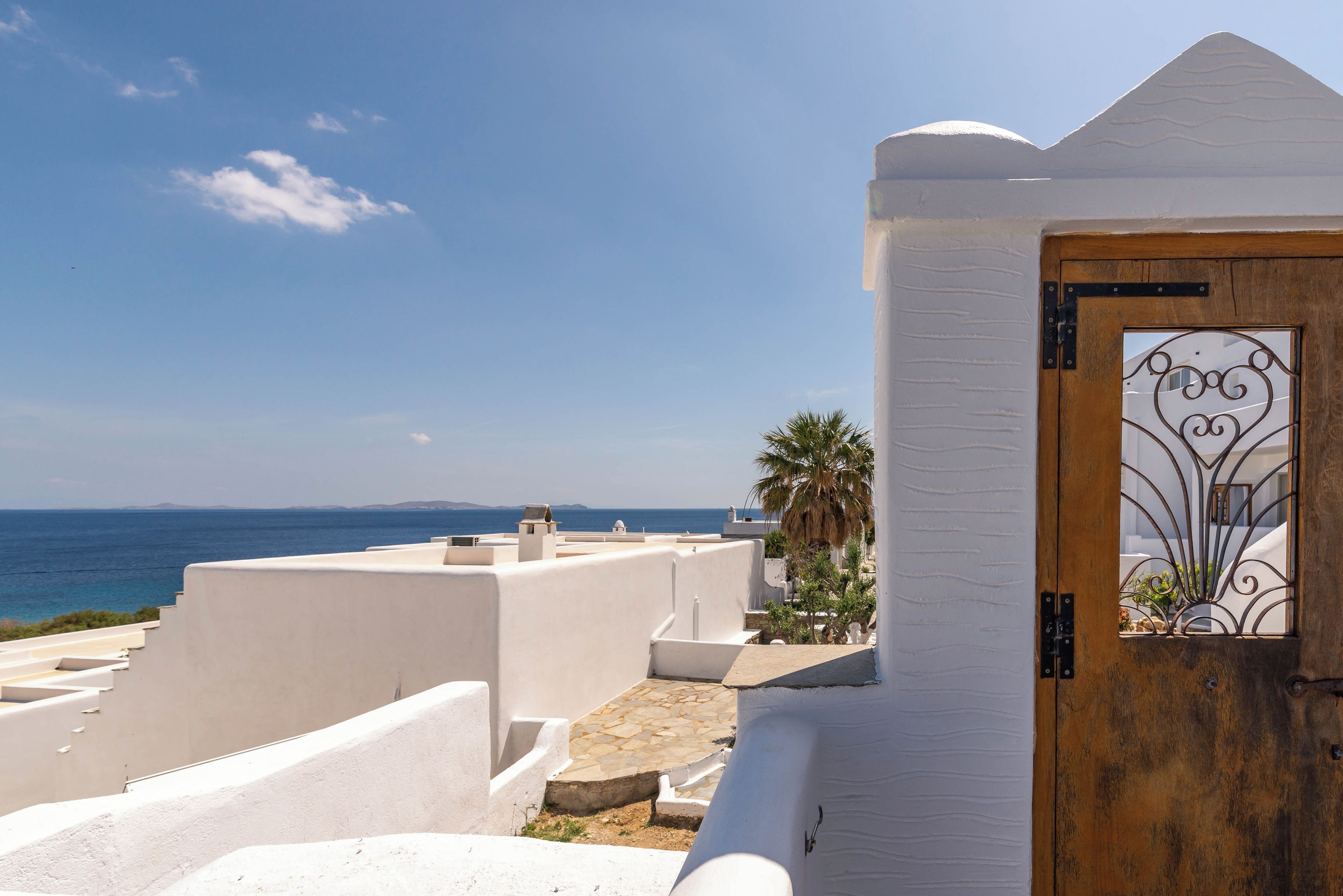 A coastal building with a white facade, a wooden door with a metal gate, and a view of the sea.