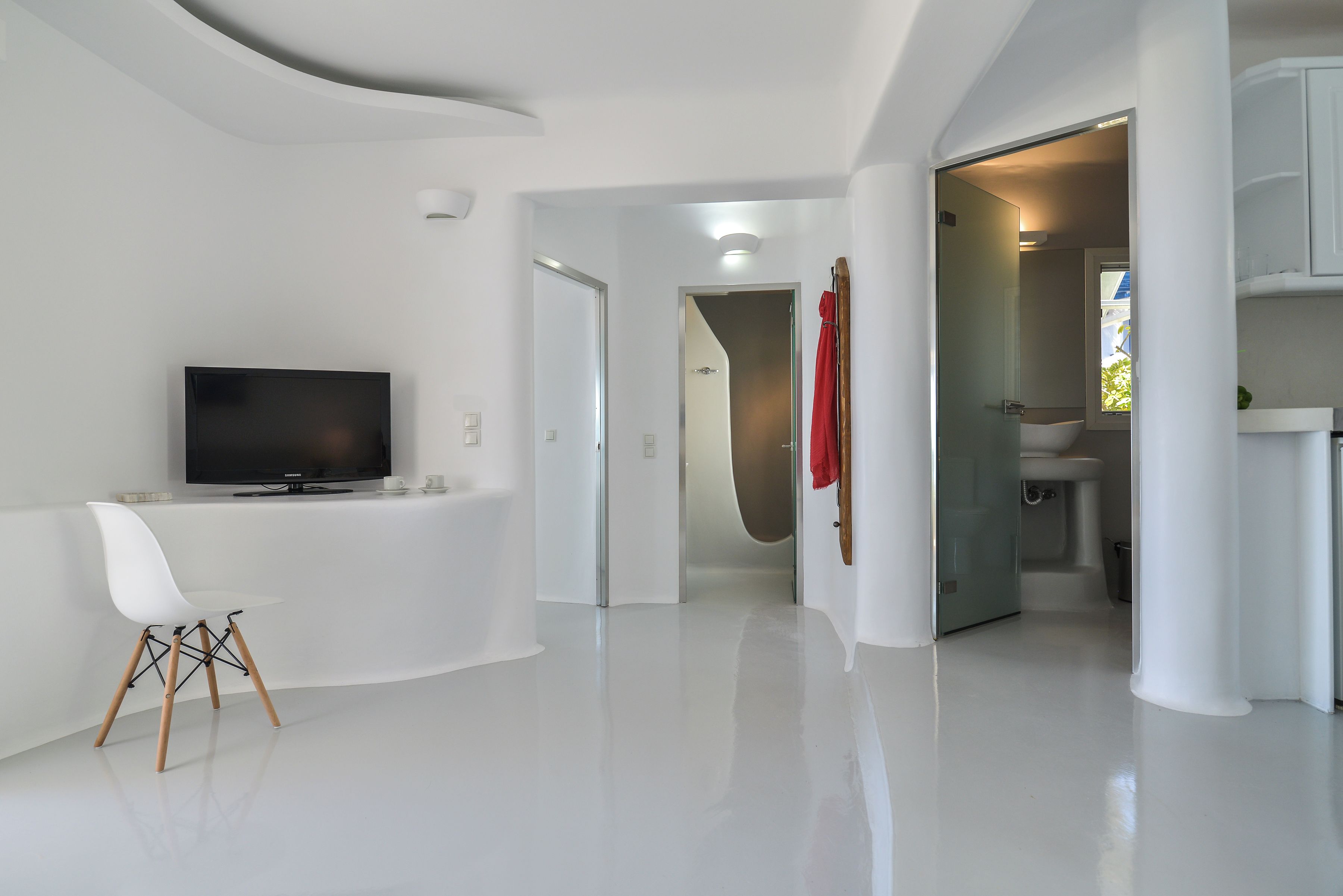 A modern interior with a flat-screen TV, a white chair, and a glass door leading to a bathroom.