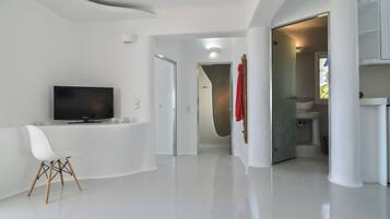 A modern interior with a flat-screen TV, a white chair, and a glass door leading to a bathroom.