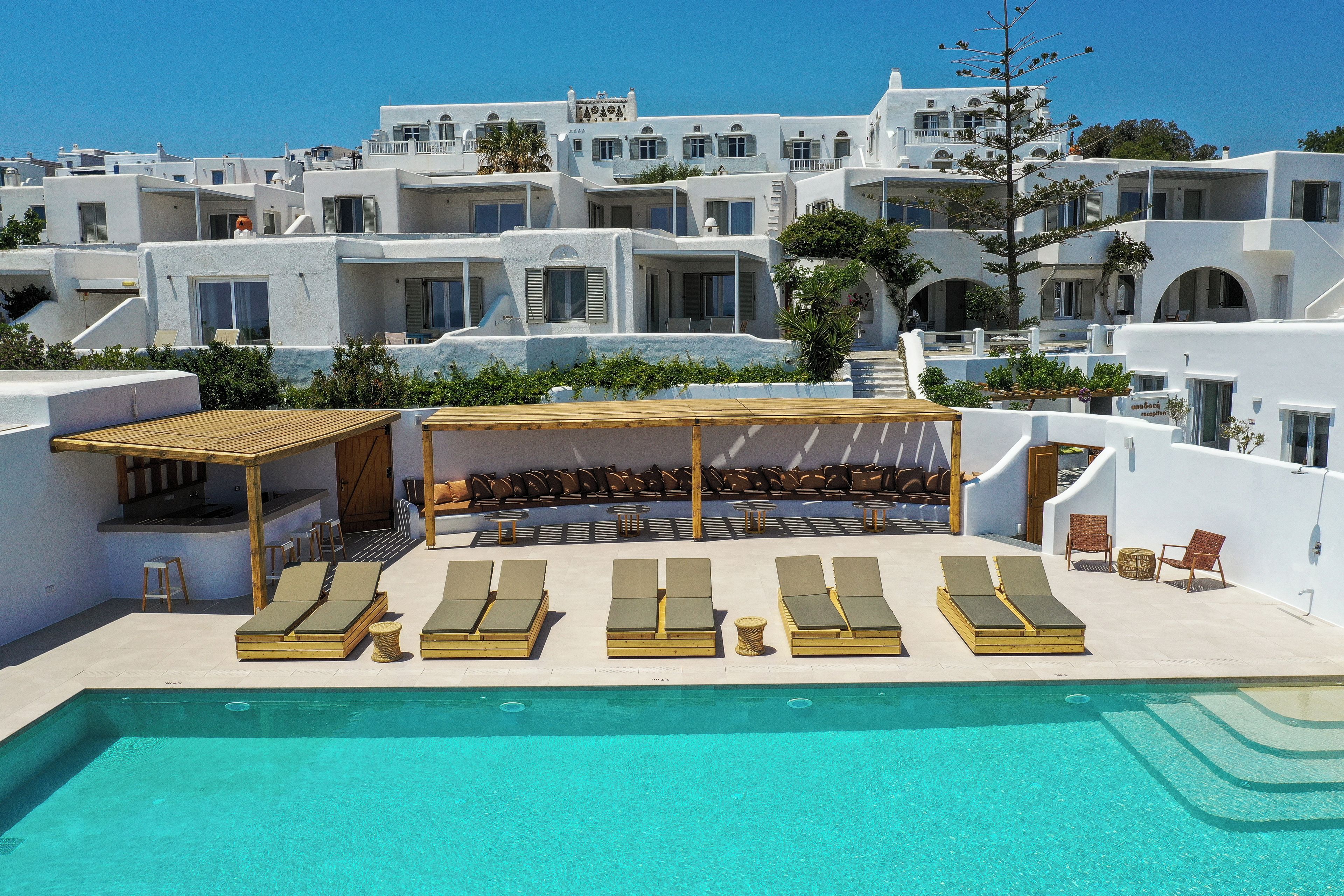 A poolside area with sun loungers and a covered seating area, surrounded by white buildings with balconies.