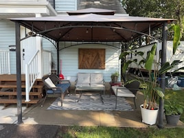 A covered patio area with outdoor furniture, a patterned rug, and potted plants.