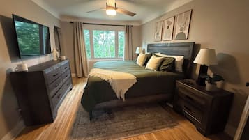 A bedroom with a bed, dresser, nightstand, lamp, ceiling fan, and a TV.